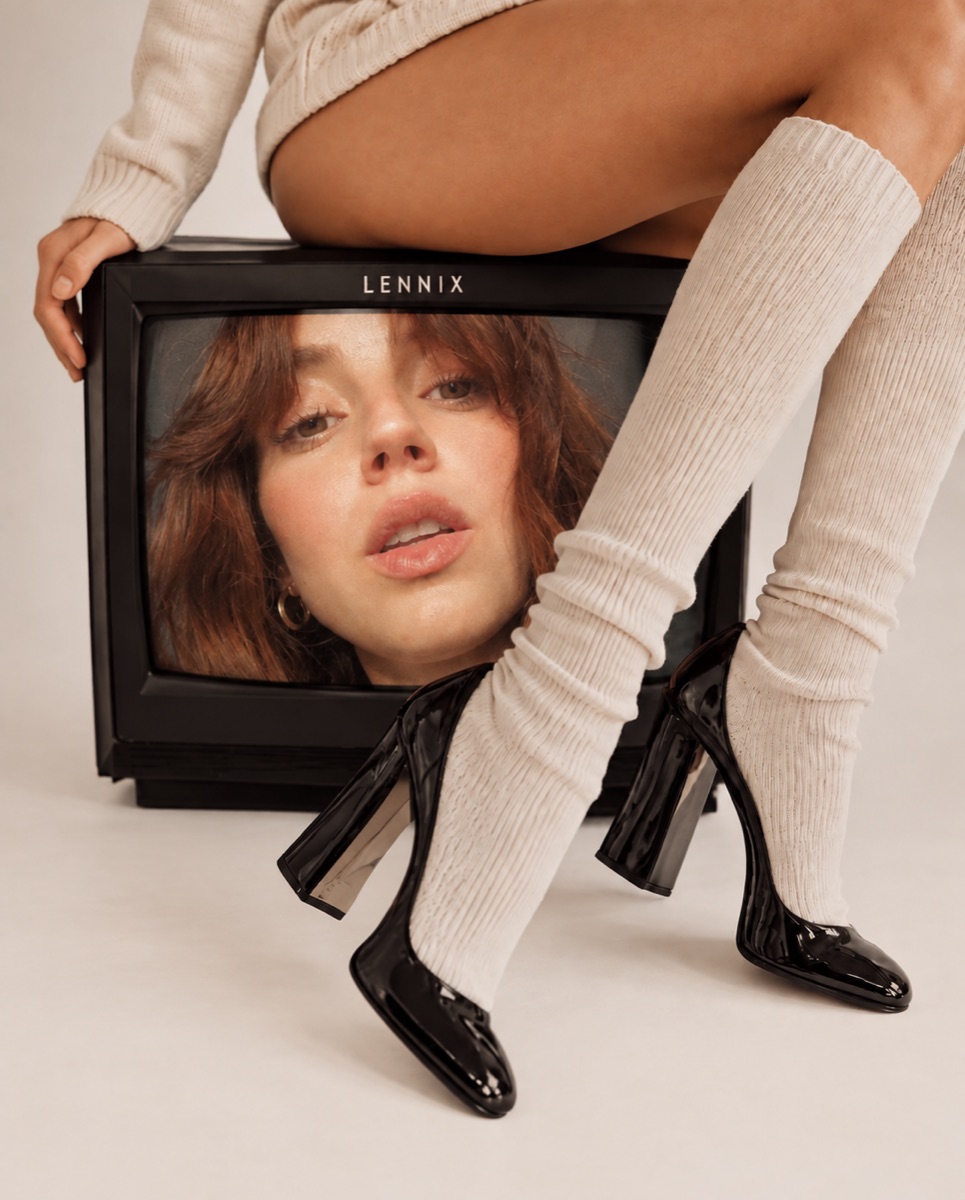 Mujer sentada sobre un televisor antiguo que muestra un rostro