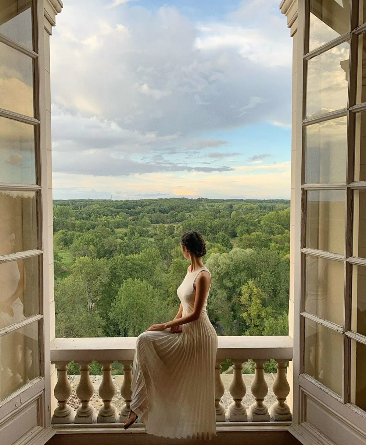 Mujer de vestido blanco sentada en un balcón, mirando el paisaje
