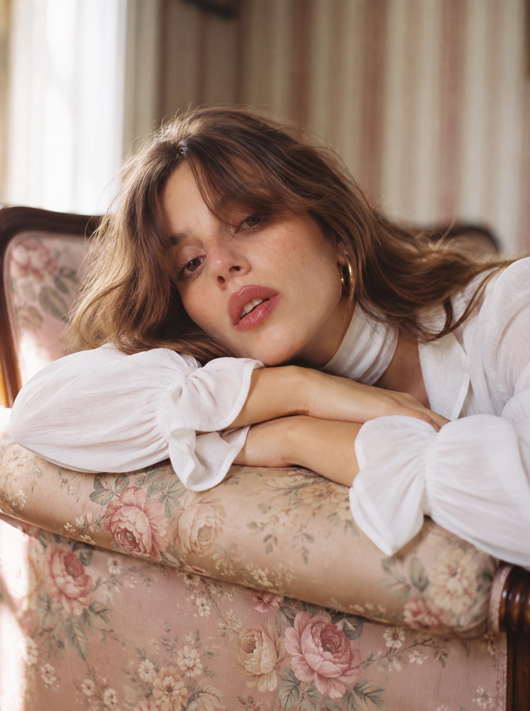 Mujer de blusa blanca apoyada sobre un sillón floreado